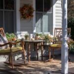 Fall porch decor with wooden chairs, pumpkins, and mums near a white porch post