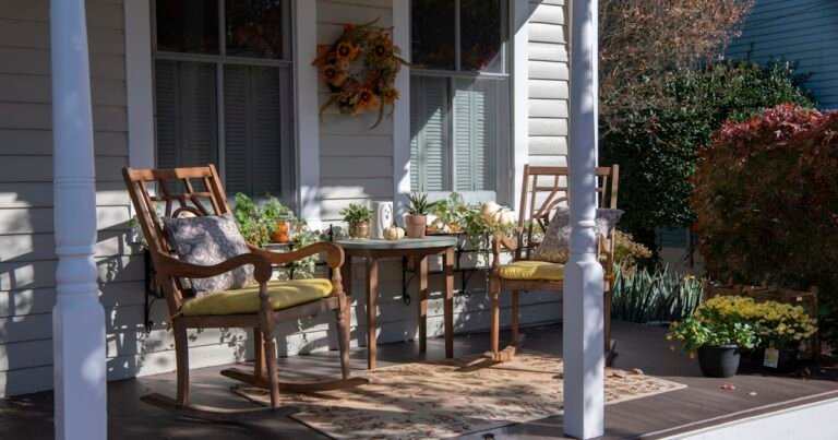 Fall porch decor with wooden chairs, pumpkins, and mums near a white porch post