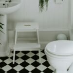 Bathroom decor ideas on a tight budget: a small white bathroom with a pedestal sink, potted plants and a black-and-white checkered floor