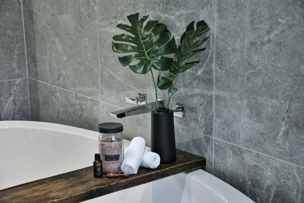 A white bathtub with soap bottles and a green plant on the ledge, a budget bathroom styling idea
