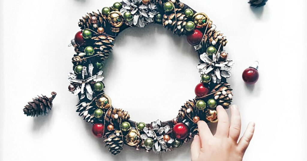 Dollar Tree DIY Christmas decorations: hands building a wreath from pinecones and red and gold baubles on a table