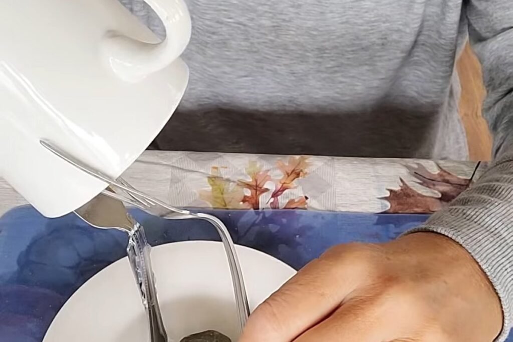 A hand holding a metal fork bent in the middle above a white saucer