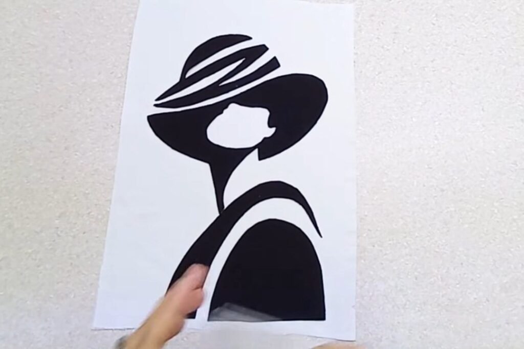 Black fabric shapes arranged on a white fabric panel in the form of a woman in a hat