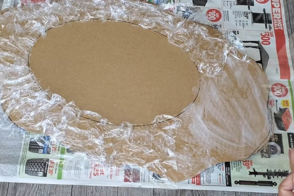 A cardboard shape with an oval centre and a thick border fully covered with crinkled clear plastic wrap