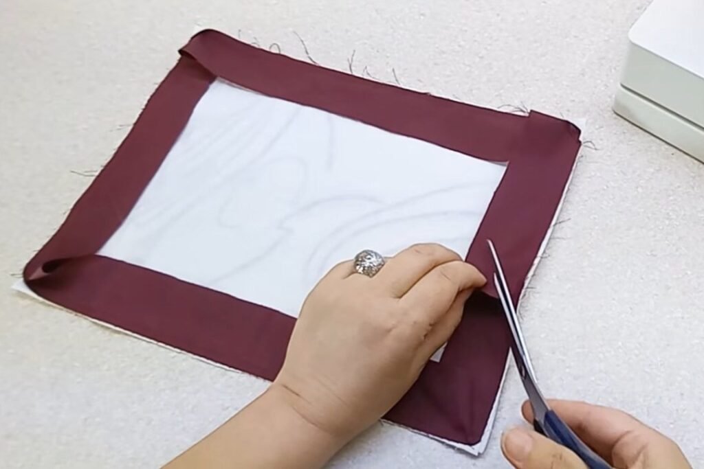 A white panel with a maroon border strip and neatly folded corners, with scissors cutting a corner