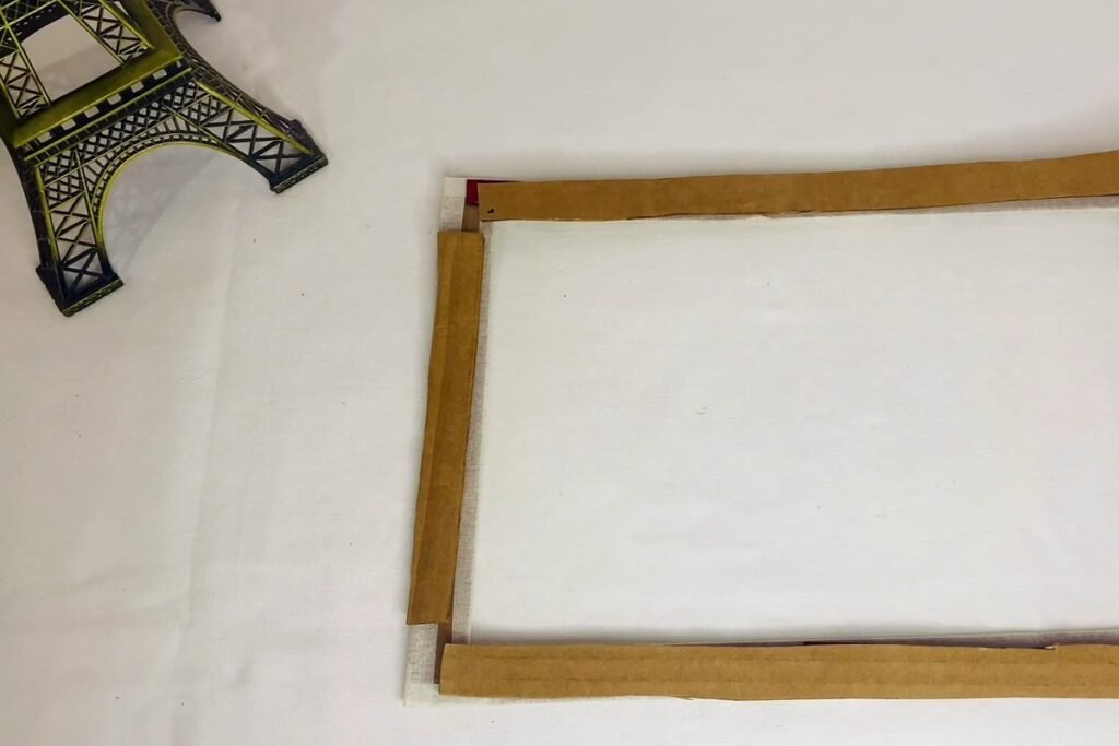 Four brown cardboard strips stuck along the sides of a frame ring over clear plastic