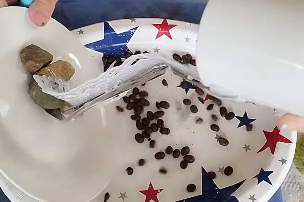 Coffee beans scattered on a large tray beneath a tilted white cup and glue ribbon
