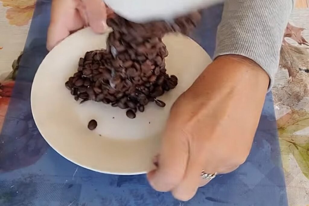 Coffee beans building up in a pile on a white saucer under a white cup