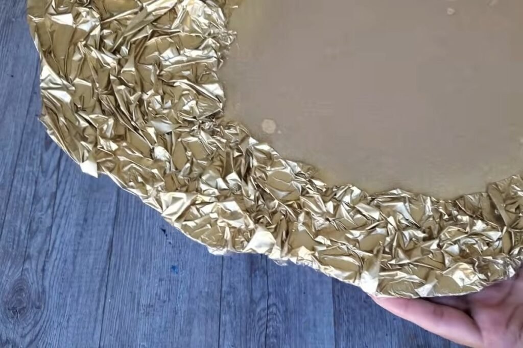 A close view of a crinkled, hammered-looking frame painted in shiny metallic gold with a bare oval in the middle