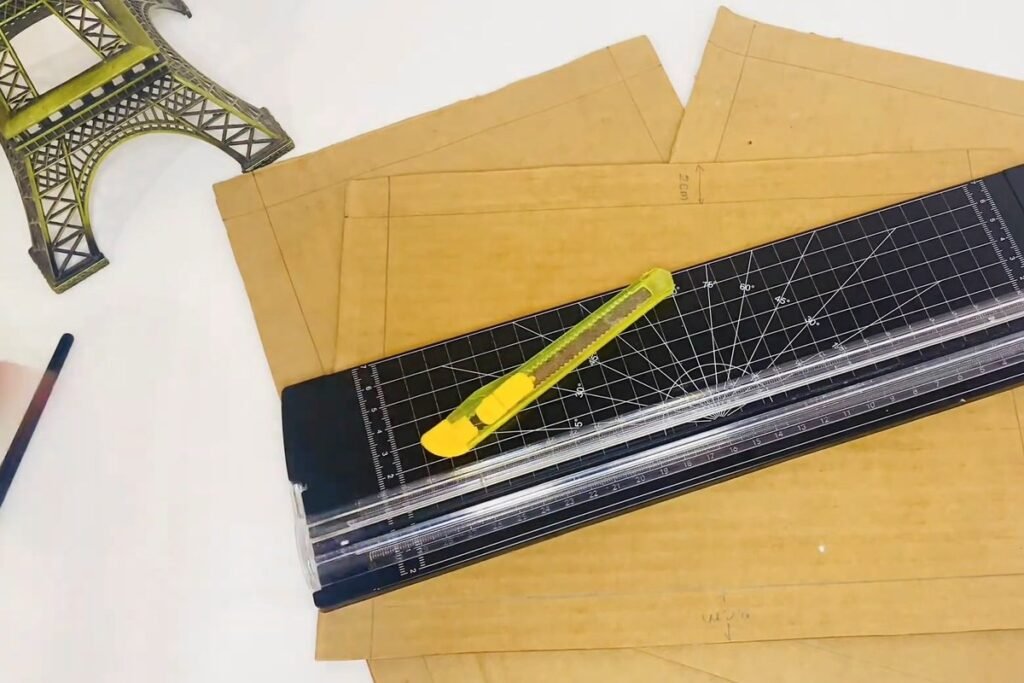 A paper trimmer and a yellow craft knife lying on marked cardboard sheets