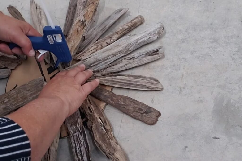 Hot glue gun adding glue where two driftwood pieces touch near the centre