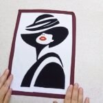 DIY fabric wall decor finished: a white fabric panel with a black applique woman in a wide hat, red lips and a thin maroon border