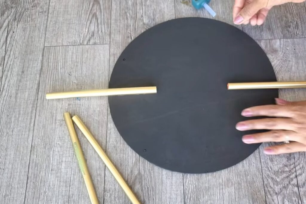 A black circle with two gold straws glued opposite each other on the horizontal line and a hand resting on the board