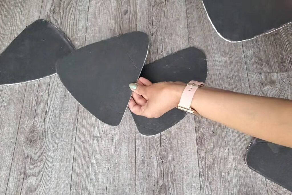 Several black foam board shapes shaped like rounded triangles laid out on a wooden floor with a hand placing one