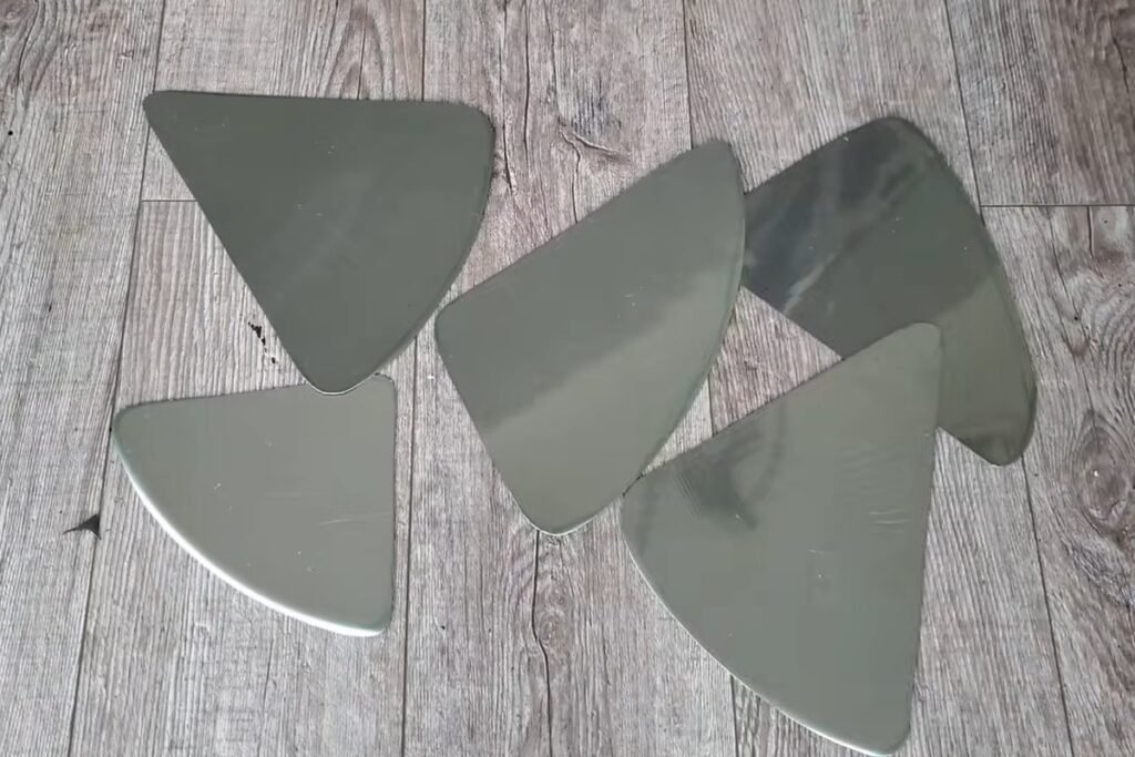 Five shiny metal pieces shaped like triangles with rounded corners laid out on a wooden floor