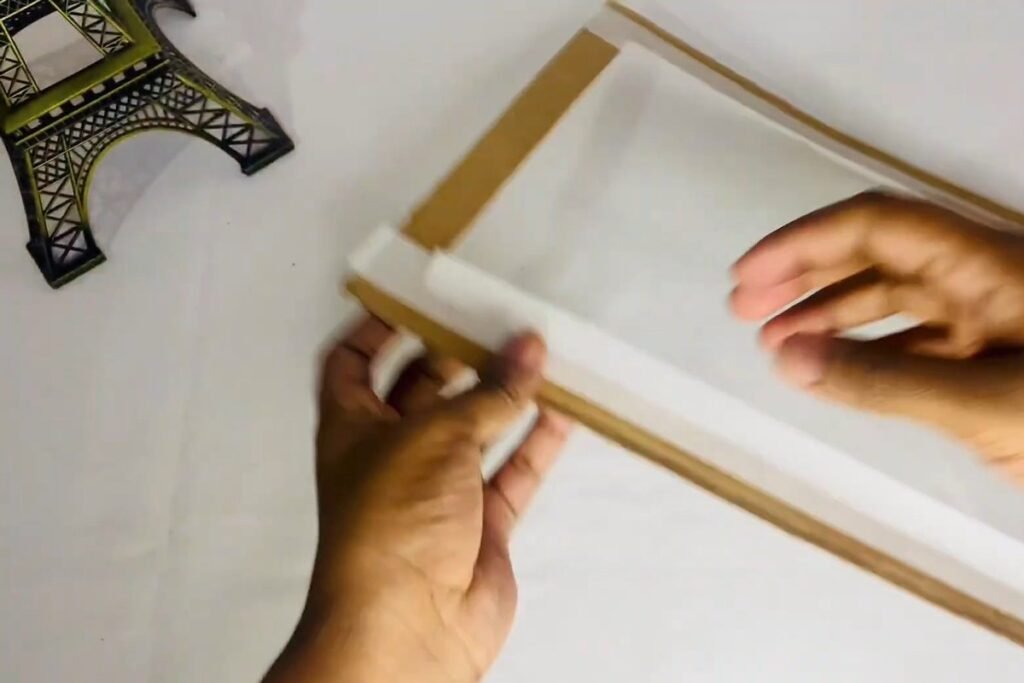 Hands folding masking tape over the edge of a cardboard frame ring