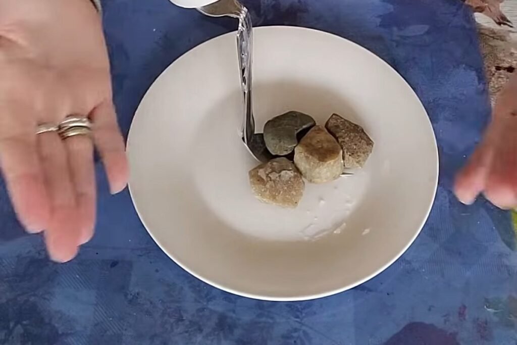 A white saucer with a fork standing up from a pile of pebbles glued around its base