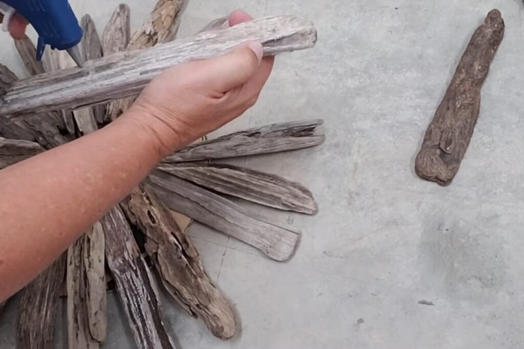 Hand holding a driftwood arm next to a hot glue gun