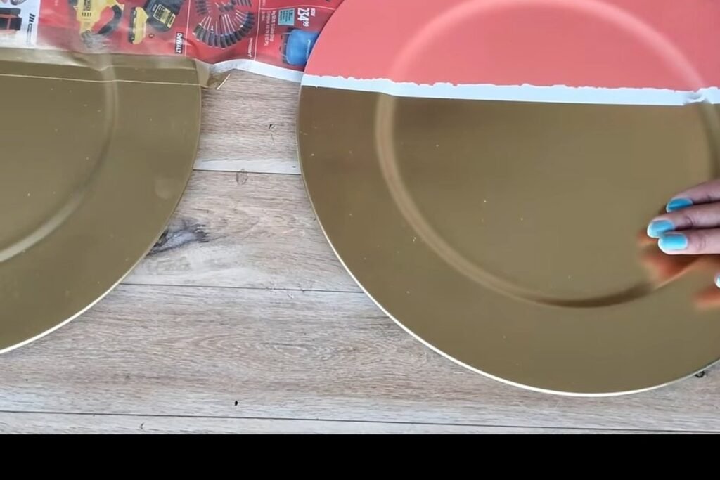 A large plate with a coral top half and a metallic gold bottom half on a wooden floor, with a hand at the edge