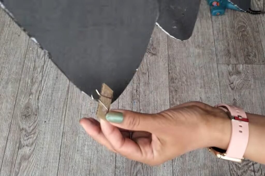 The back of a black foam piece with a small wooden hanger being pressed on by a hand