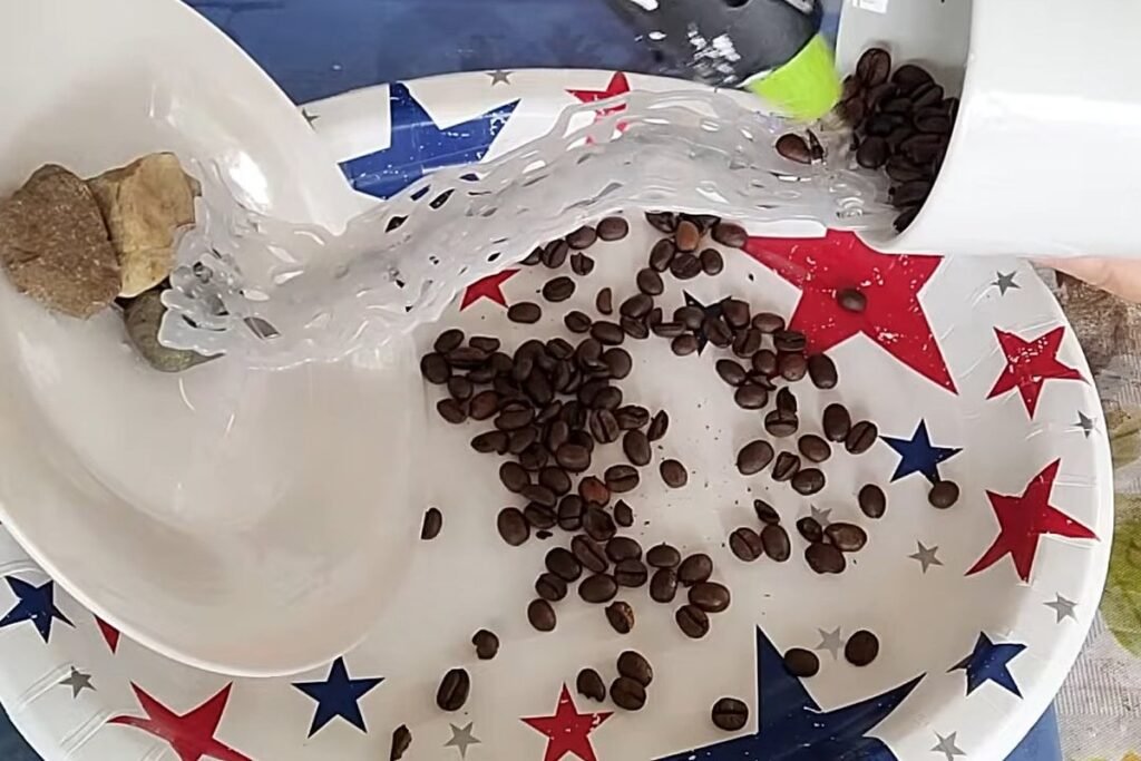 A hot glue gun on a white cup while coffee beans are poured over the glue