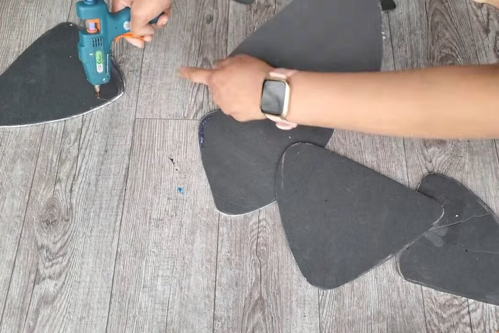 A hot glue gun running a line of glue along the edge of one black foam shape touching another