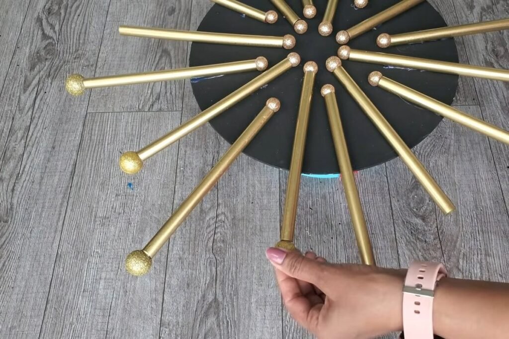 Gold straw rays with large gold glitter balls glued on the outer tips and a hand holding the last ball