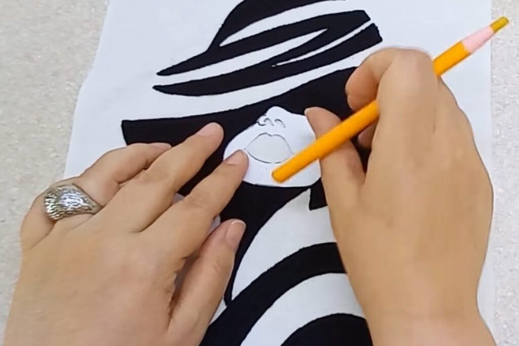 A hand holding a paper face piece over the face gap on the fabric portrait and marking with an orange pencil