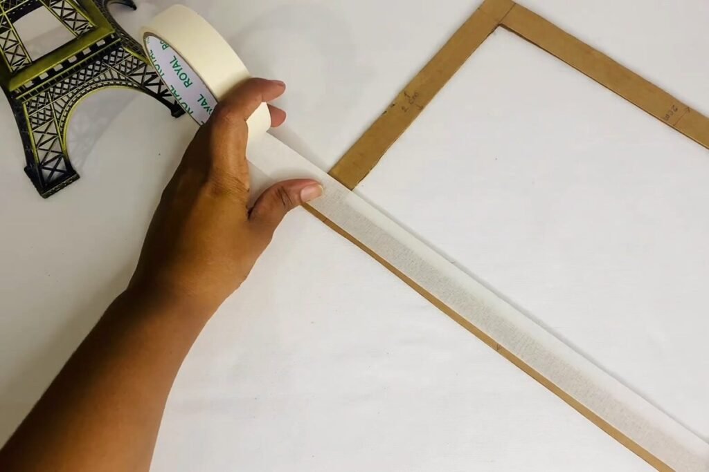 Hand laying a strip of masking tape along the edge of a cardboard frame ring