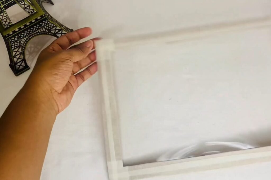 Hand holding a frame with masking tape pressed around the edges of the clear plastic