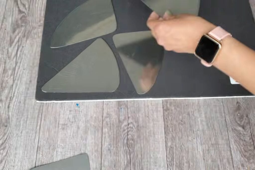 Several shiny metal triangle pieces arranged on a black foam board with a hand moving one into place