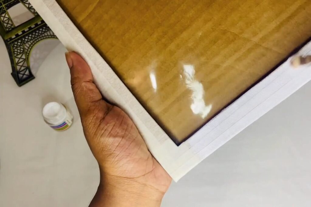 Hand holding a taped frame at an angle while white paint is brushed along the edge