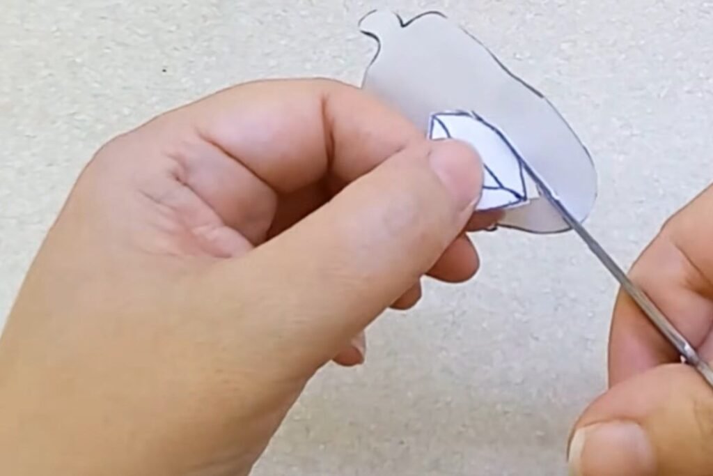 A hand cutting a small paper face shape with small scissors