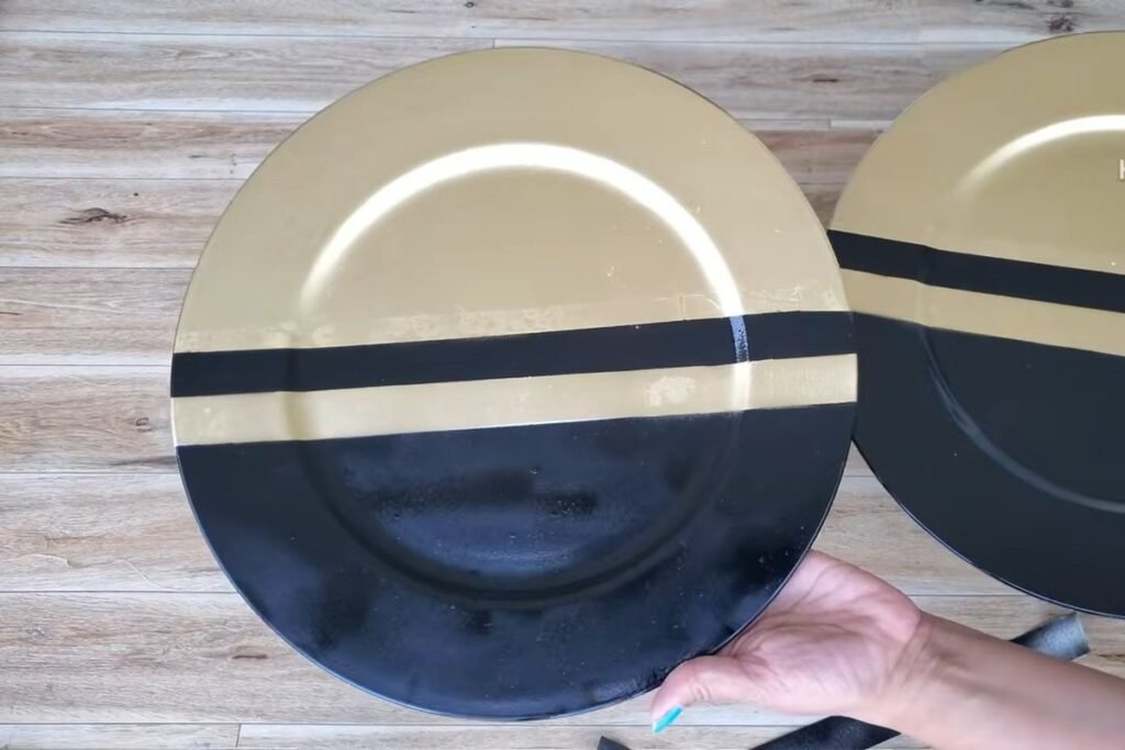 Two large plates, one black on the bottom half with a gold stripe and a gold top half, held by a hand