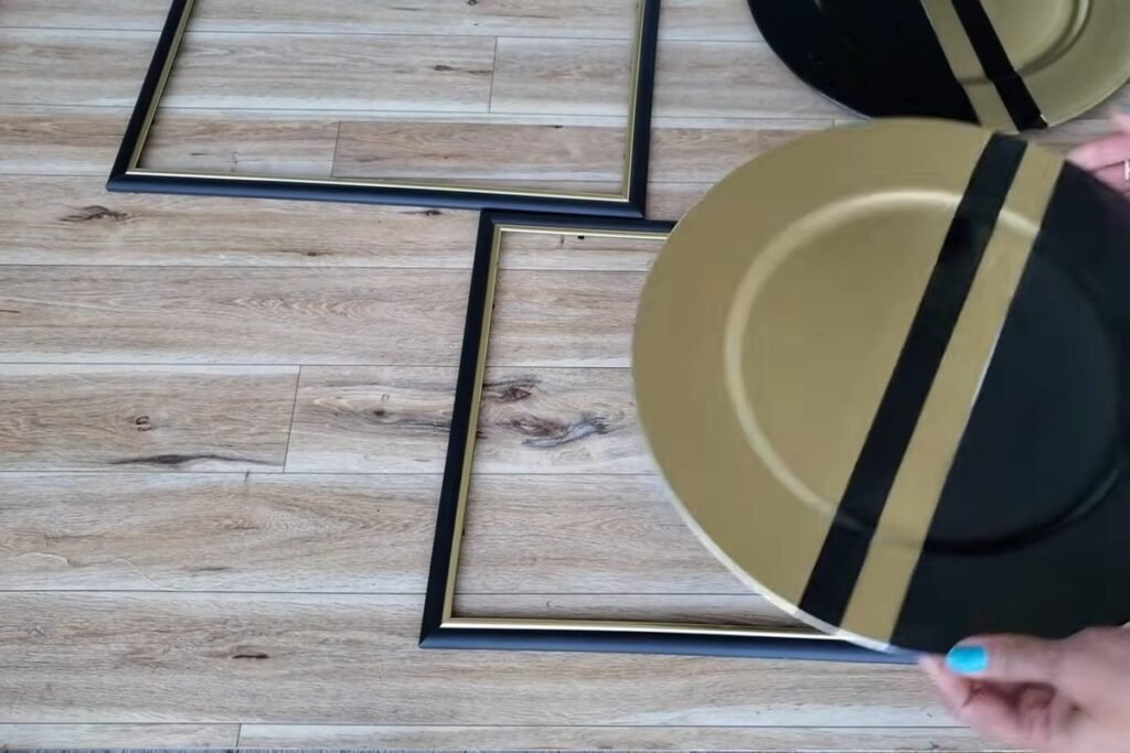 A gold and black striped plate laid over an empty picture frame with a second frame and plate beside it