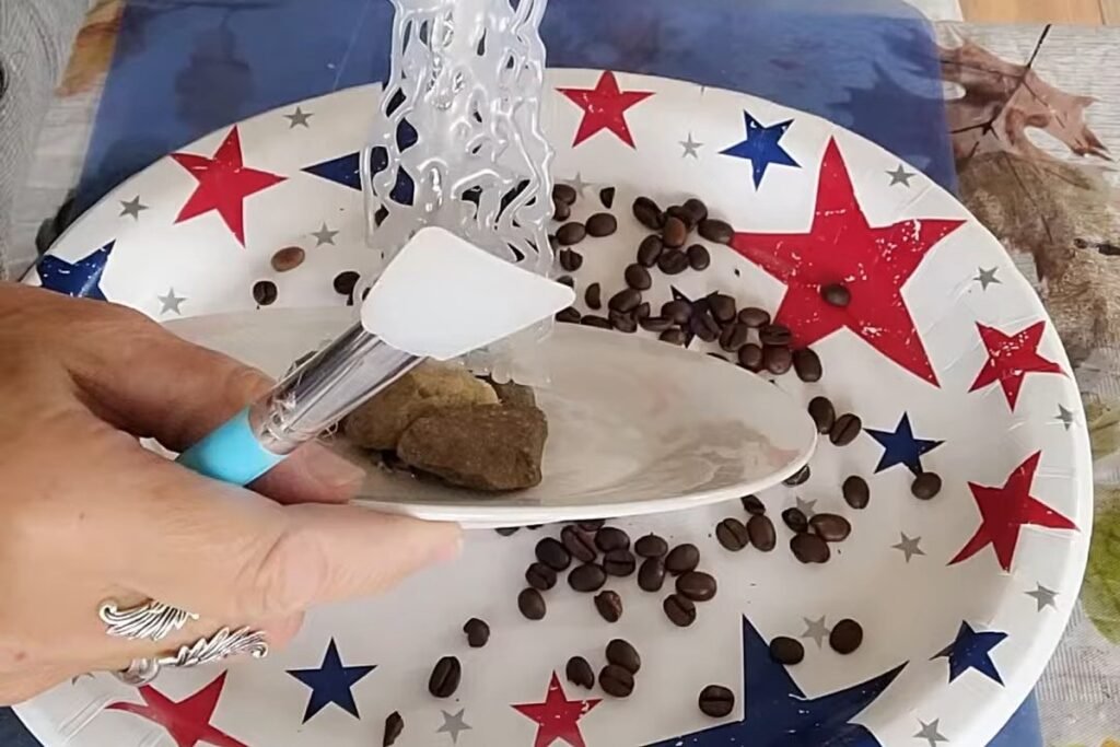 A hand pressing coffee beans into glue with a small tool that has a blue handle