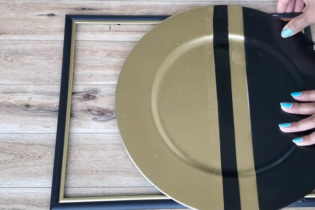 A large gold and black plate with a vertical black stripe pressed down onto a picture frame by two hands