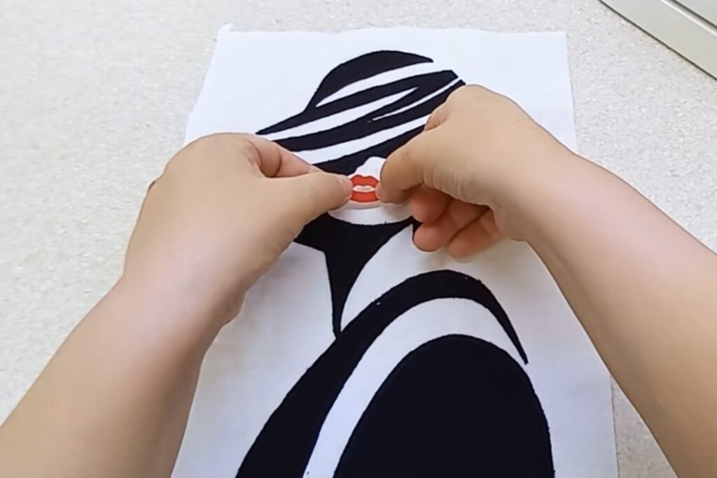 Both hands pressing a small pair of red lips onto the face opening of a fabric portrait