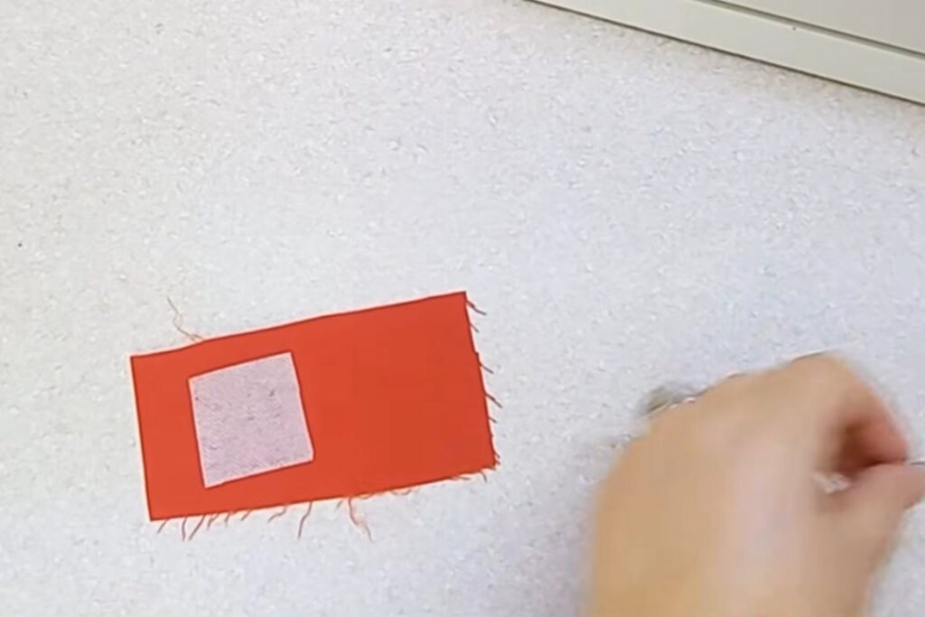 A scrap of red fabric with a small square of white interfacing lying on top of it
