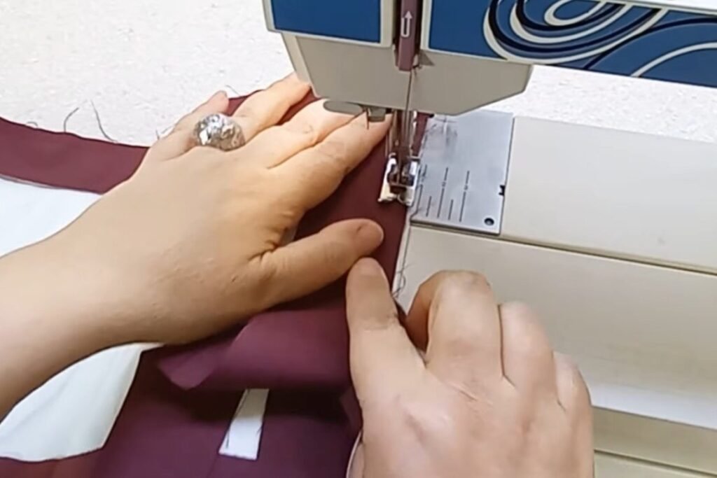 A sewing machine stitching a maroon fabric strip along the edge of a white panel