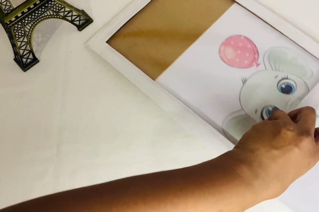 Hand sliding a printed elephant picture into a white frame between the plastic and the back sheet