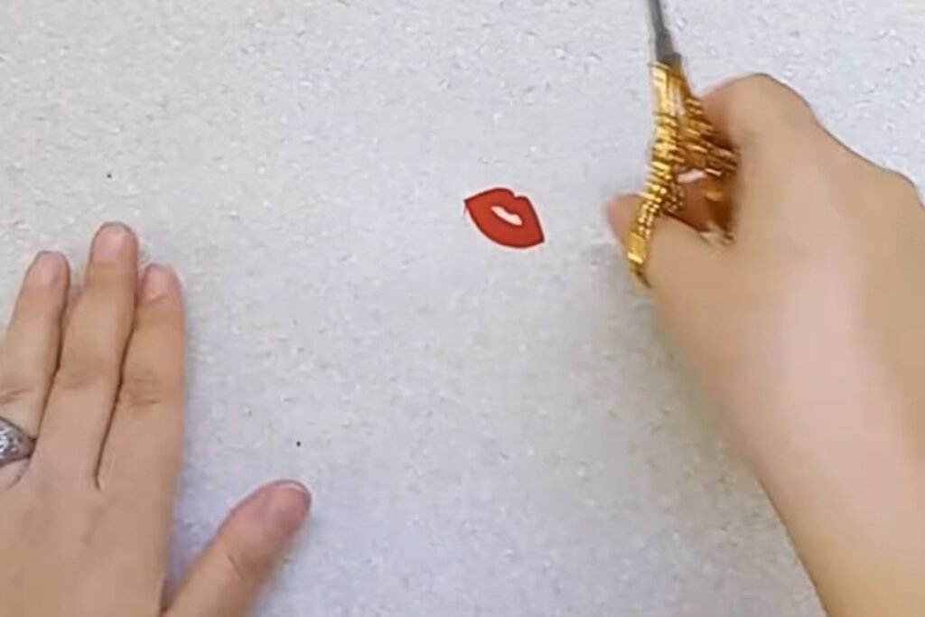 A tiny pair of red fabric lips on a table next to gold-handled scissors