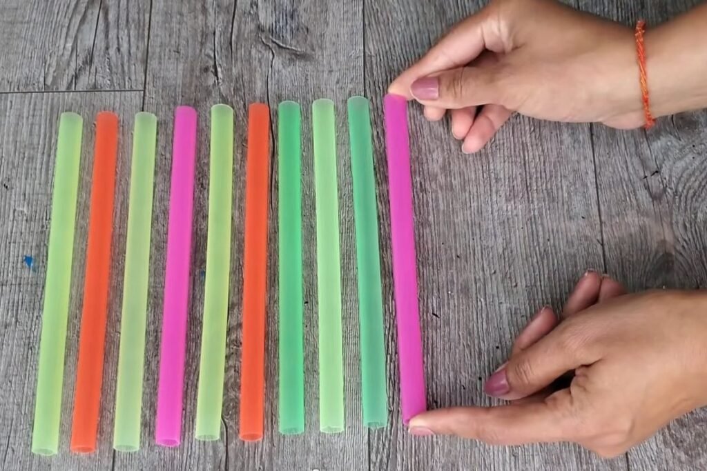 Jumbo straws in green, orange and pink laid side by side in a row with two hands holding the edges