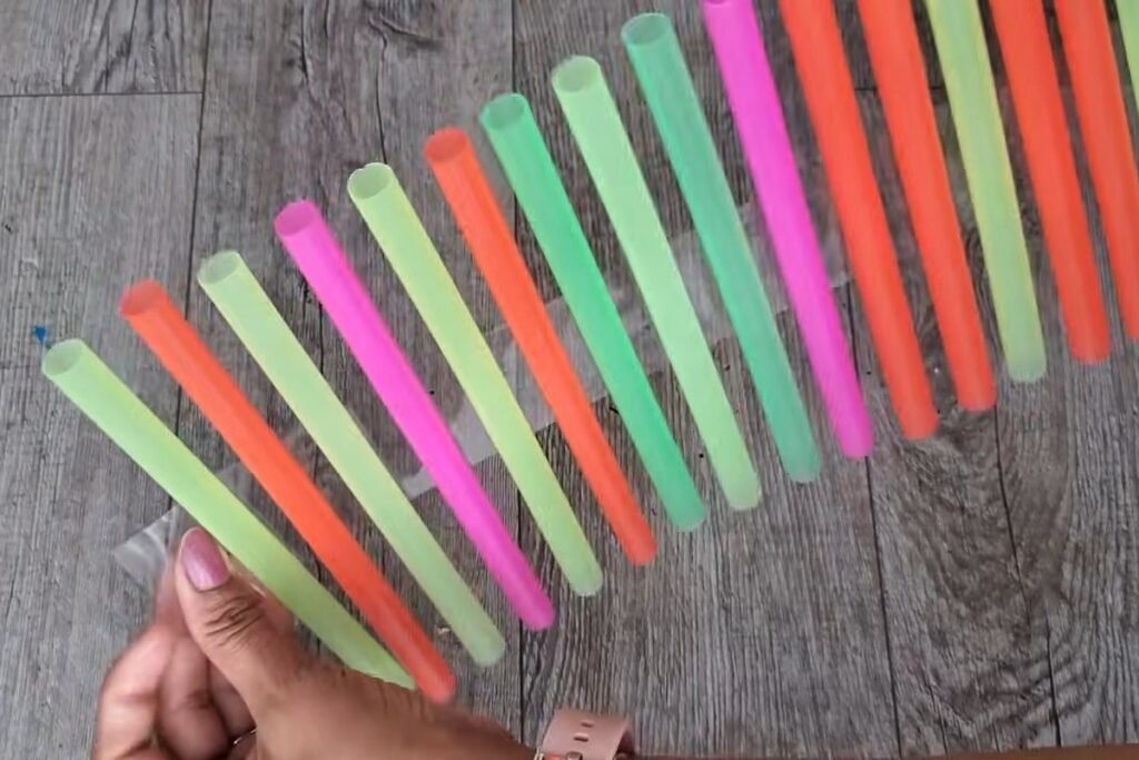 A flat strip of colored straws held together by clear tape, lifted slightly by a hand