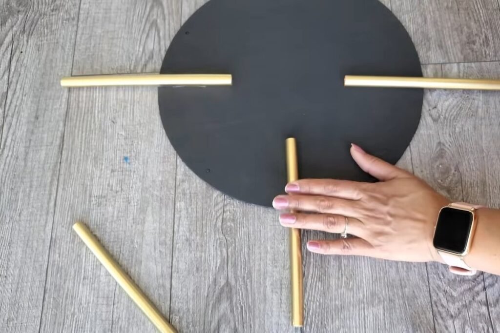 A black circle with gold straws laid out in a plus shape and a hand placing the third straw