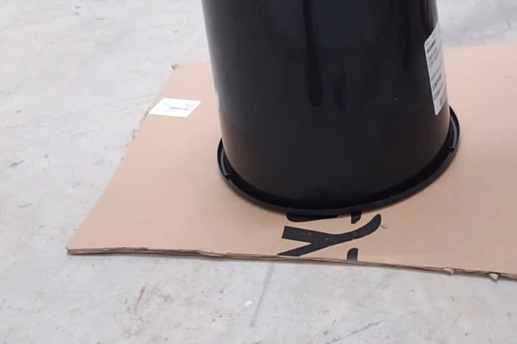 A black bucket upside down on a sheet of cardboard, ready to trace a circle