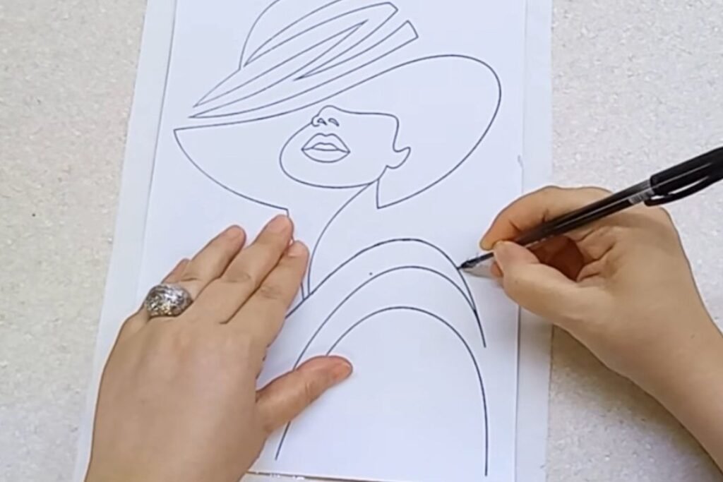 A hand tracing the lines of a hat and shoulder outline with a black ballpoint pen