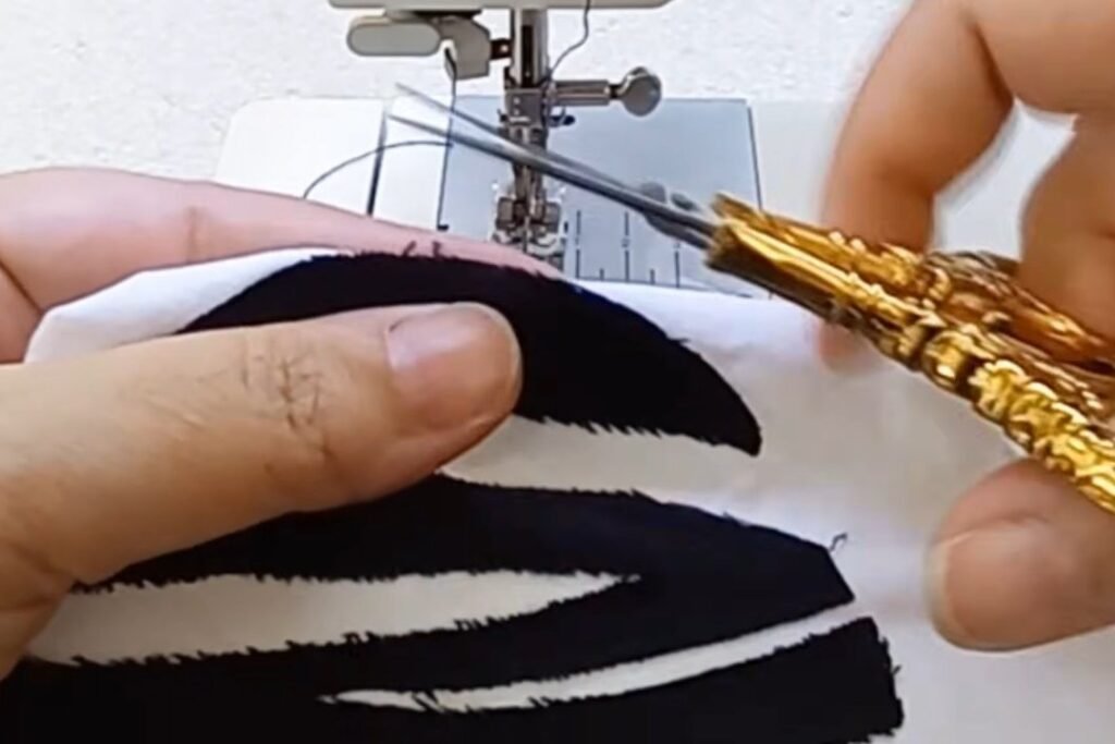 Small gold-handled scissors trimming loose threads beside a black stitched shape