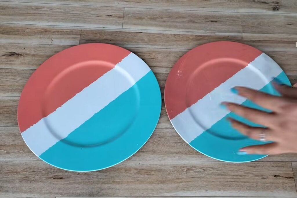 Two large round plastic plates painted in coral, white and teal bands lying on a wooden floor