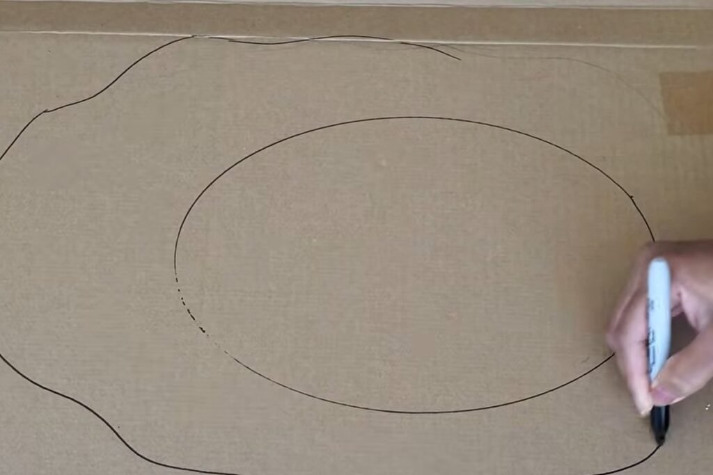 A cardboard sheet with an inner oval and an irregular wavy outer line drawn around it in black marker